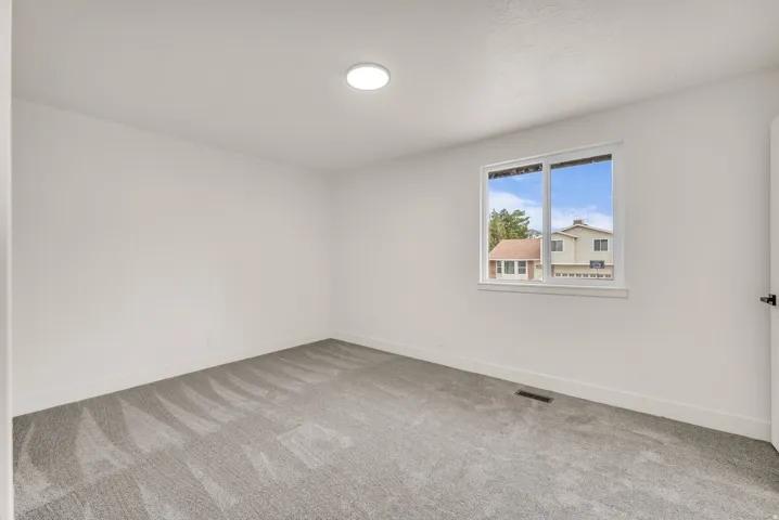Recessed ceiling light, neutral wall paint, gray patterned carpet, white window trim, and white baseboards