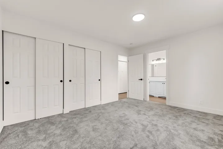 White walls, gray carpeting, and multiple panel doors with matte black hardware