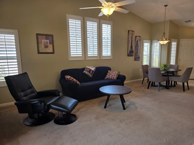 Vaulted ceilings with a ceiling fan, multiple windows with white plantation shutters, and a brass-tone chandelier