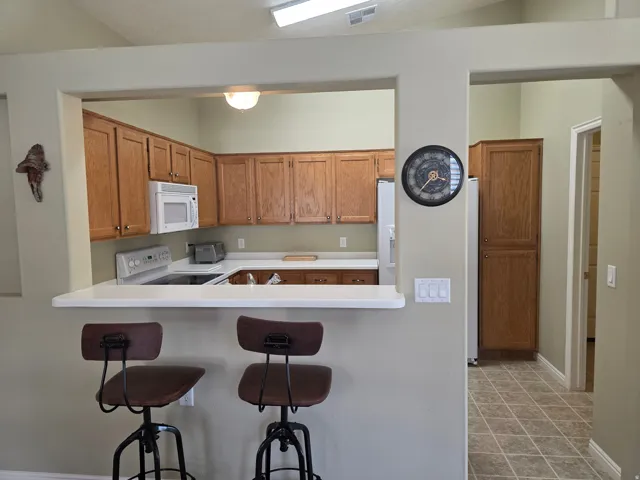 Open kitchen featuring wood-finish cabinetry, a peninsula counter with seating for two, stainless steel appliances, and tile flooring