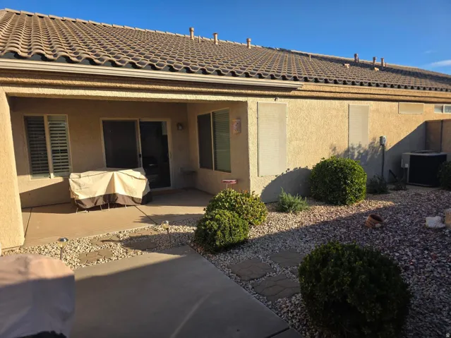 Covered patio with a concrete surface, sliding glass door, tiled roof, and a low-maintenance yard featuring gravel and established shrubs