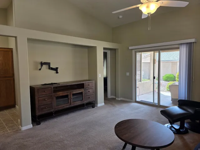 Vaulted ceiling, ceiling fan with integrated lighting, sliding glass door, built-in display niche, and carpet flooring
