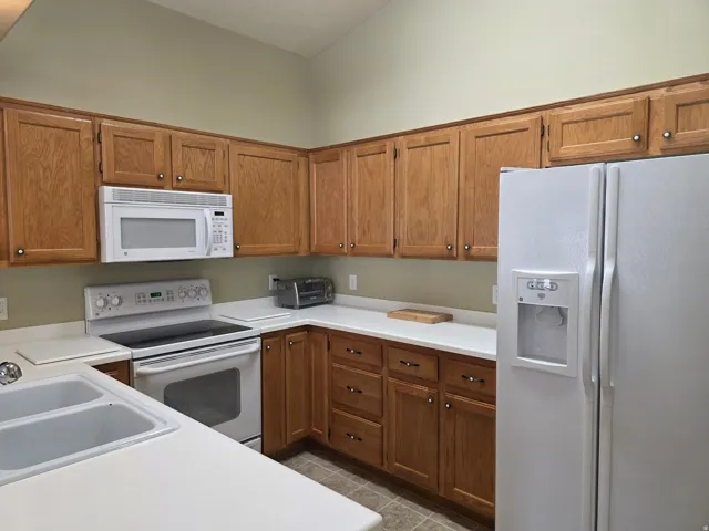 Kitchen featuring wood cabinetry, white countertops, a double basin sink, a white electric range, and a white microwave
