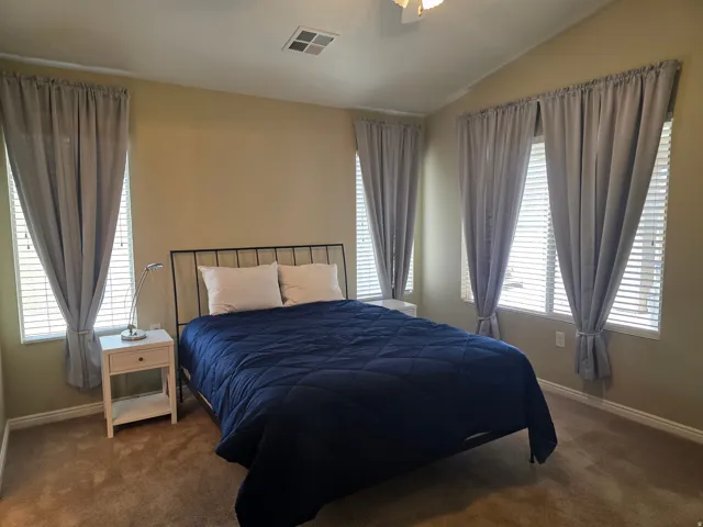 Primary Bedroom with vaulted ceiling, ceiling fan, multiple windows with blinds, and wall-to-wall carpeting