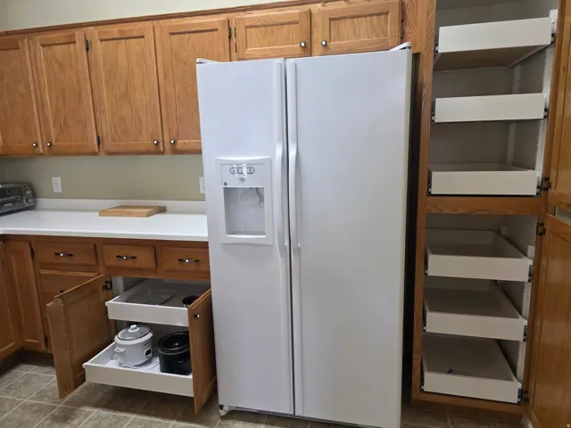Wood cabinetry with pull-out drawers, white solid surface countertops, and a tile floor