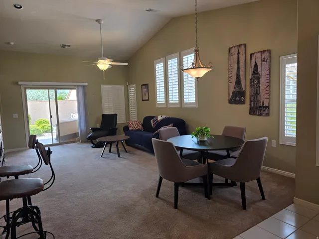 Vaulted ceiling with an attached ceiling fan, sliding glass door, multiple windows with plantation shutters, and a suspended light fixture
