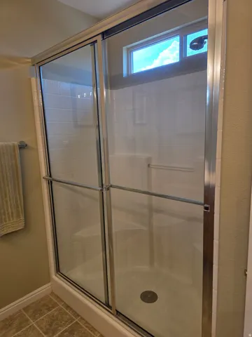 Primary Shower enclosure with clear glass sliding doors and an integrated window, featuring a built-in shower bench and a tiled floor