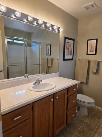 Primary Bathroom with Wood-finish vanity with white hardware, integrated sink, and light-toned countertop