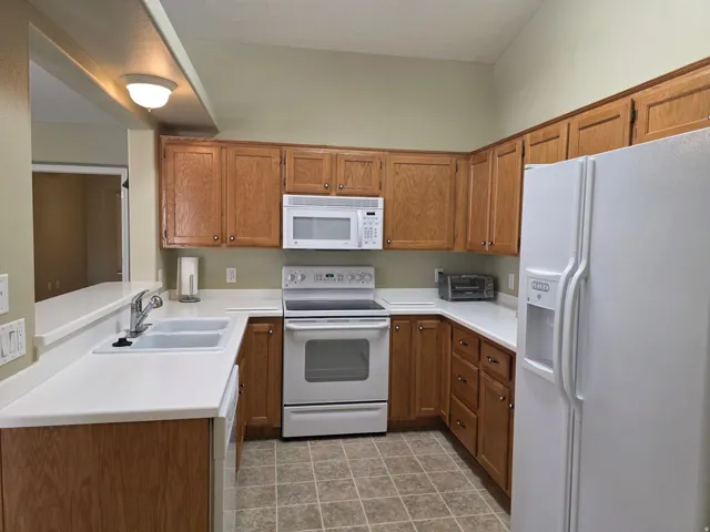 U-shaped kitchen featuring wood cabinetry, white countertops, white appliances, and a pass-through window