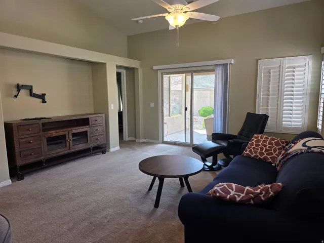 Vaulted ceilings with a ceiling fan, carpet flooring, sliding glass patio door, and plantation shutters