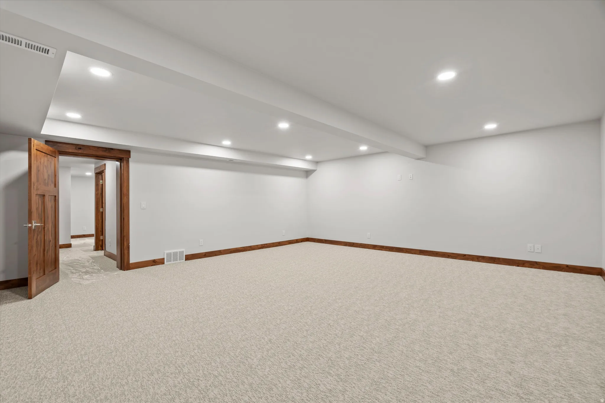 Spacious room featuring neutral carpet flooring, recessed lighting, and wood-finish trim