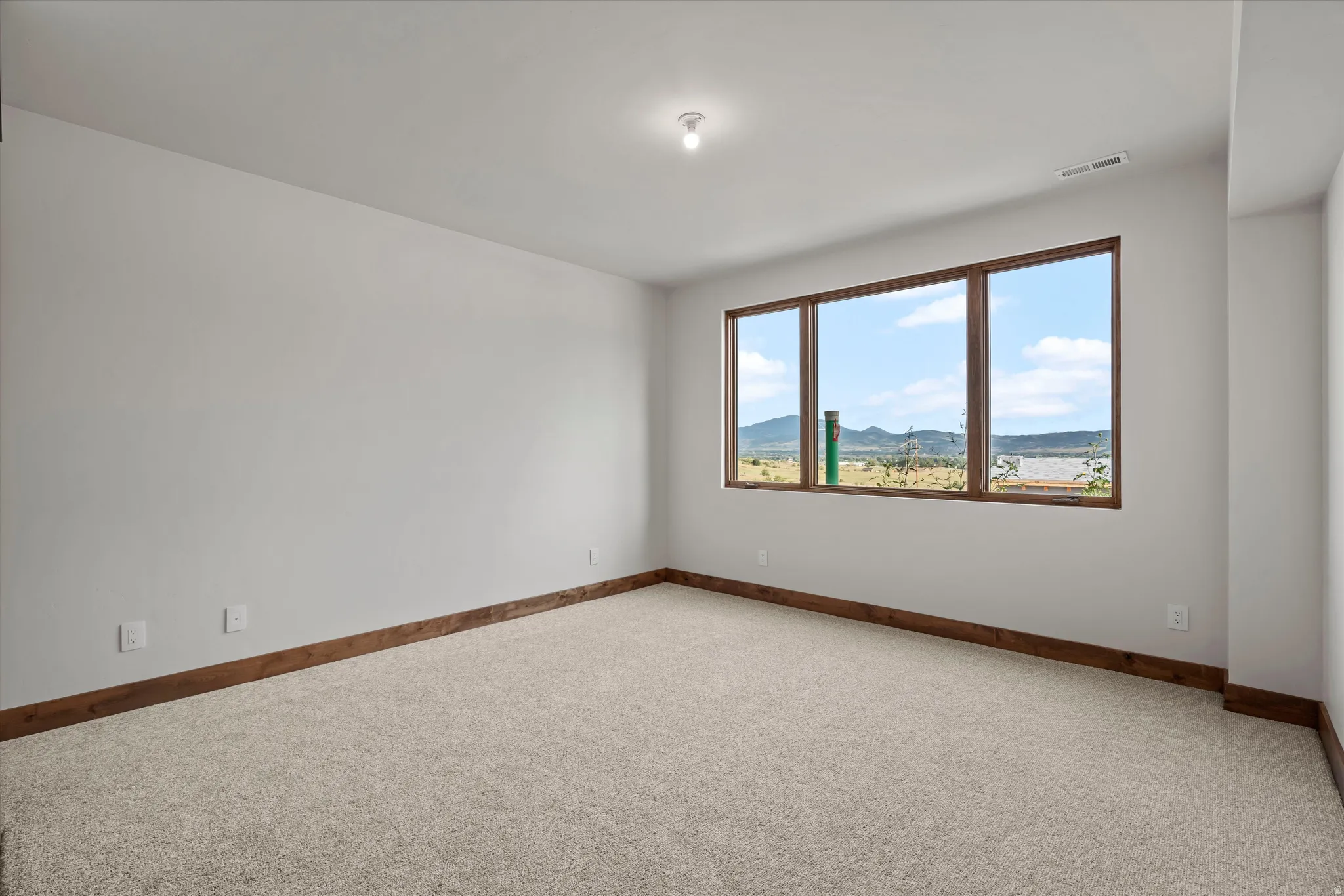 Bright corner bedroom with expansive triple-window exposure, neutral carpet flooring, and wood-trimmed architectural detailing