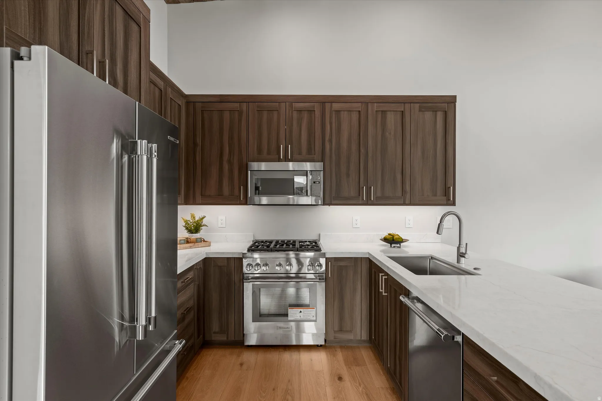 U-shaped kitchen featuring wood-finish cabinetry, stainless steel appliances, light-toned countertops, and wood-finish flooring