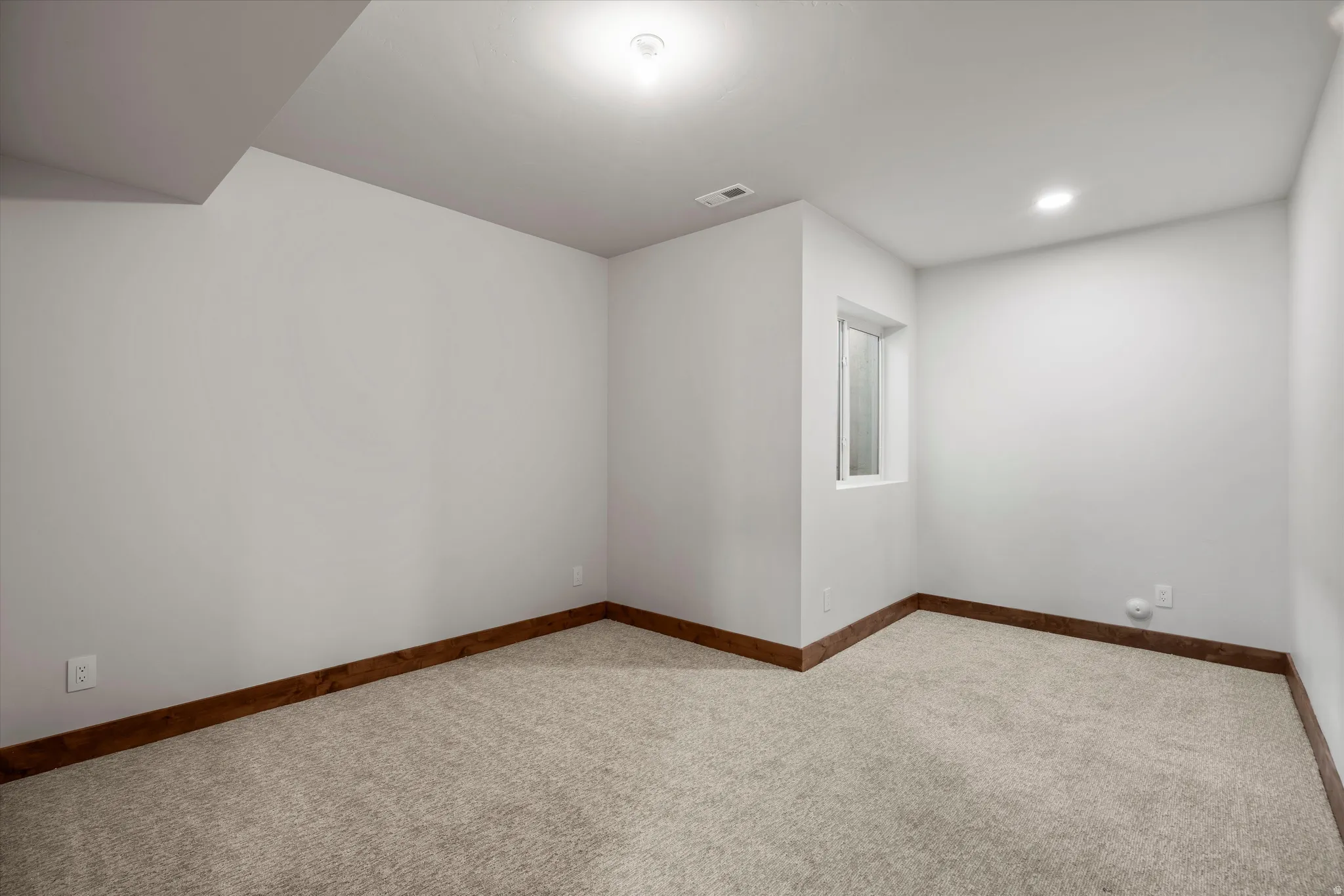 Recessed lighting, wood-finish trim, light-toned carpeting, and a window with white casing