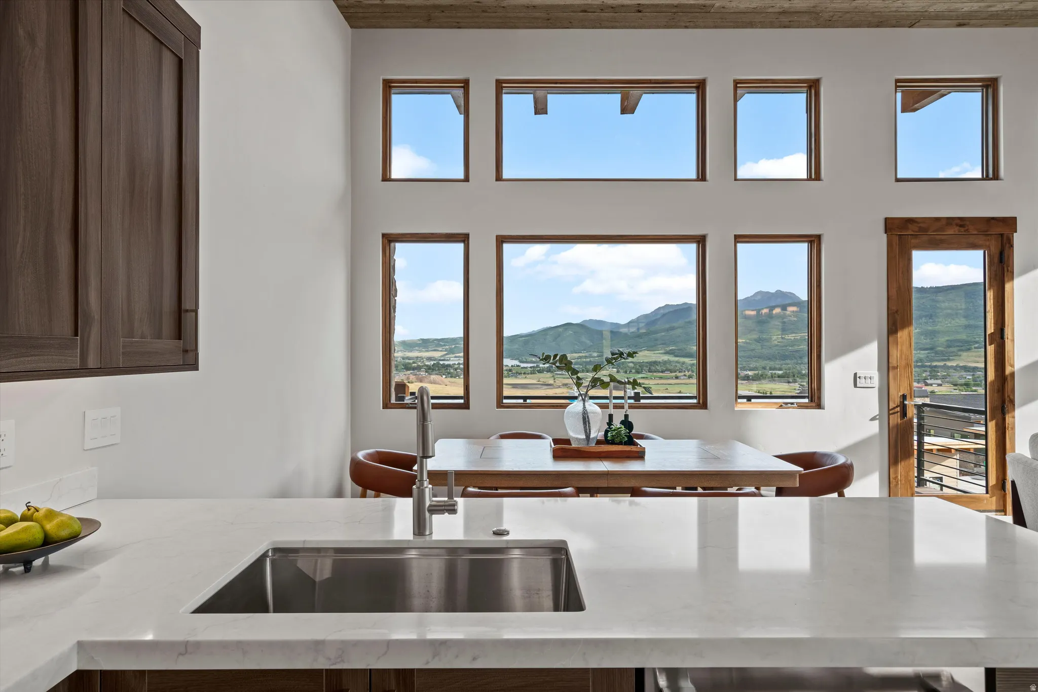 Stainless steel sink with a chrome faucet, light-toned countertop, wood-finish cabinetry, and multiple windows with wood frames