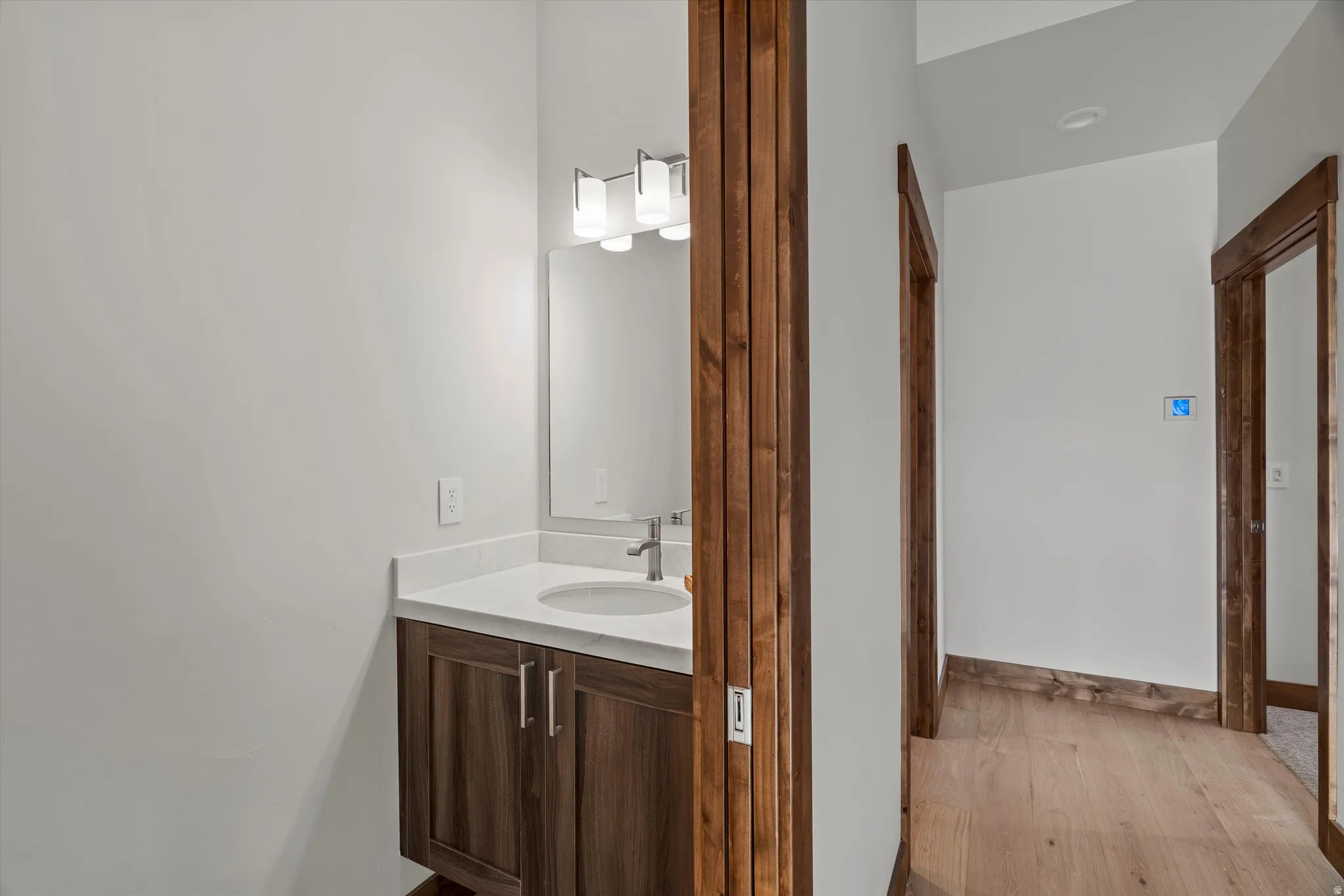 Modern bathroom vanity featuring rich wood-finish cabinetry, white countertop, and integrated sink with chrome fixtures