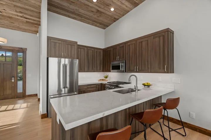 Kitchen featuring stainless steel appliances, wood-finish cabinetry, light-toned countertops, and a wood plank ceiling