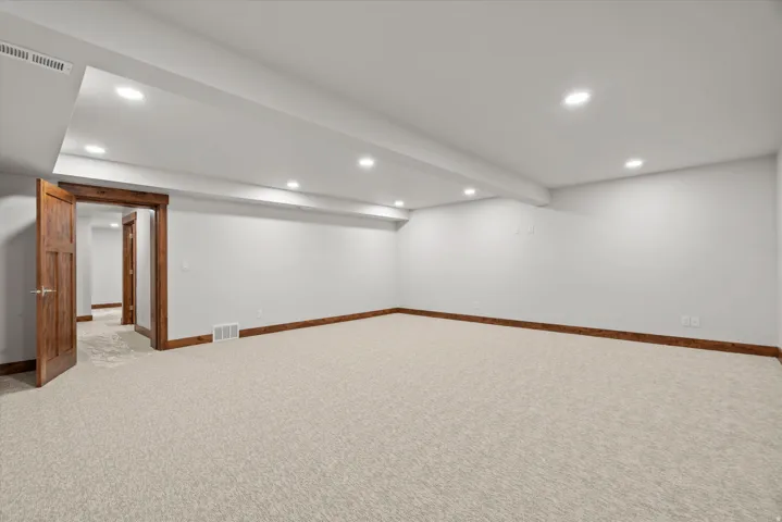 Spacious room featuring neutral carpet flooring, recessed lighting, and wood-finish trim