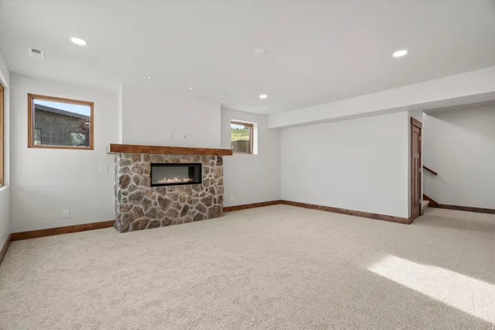 Spacious finished basement featuring a stone fireplace with wood mantel, recessed ceiling lighting, carpeted flooring, and wood-trimmed architectural details throughout