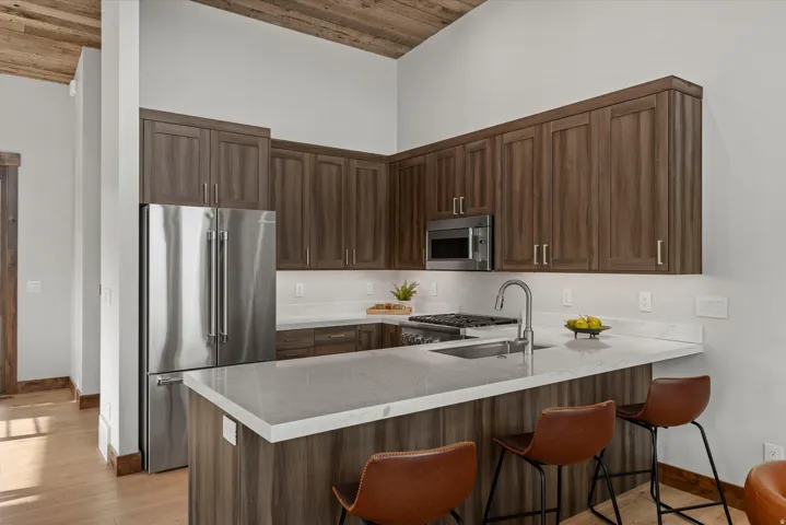 Vaulted wood-finish ceiling, stainless steel appliances, wood-finish cabinetry, light-toned countertops, and wood-finish flooring