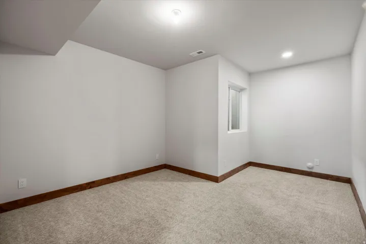 Recessed lighting, wood-finish trim, light-toned carpeting, and a window with white casing