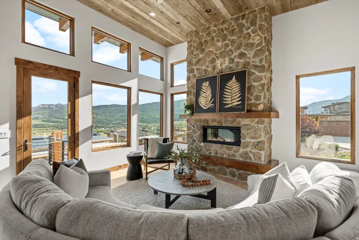 Stone fireplace with a wood mantel, wood-finish ceiling, multiple windows, and a glass-paneled door