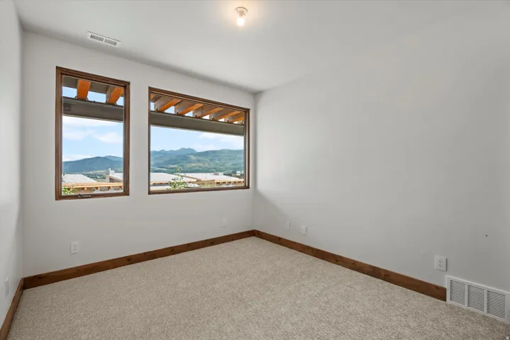 Two large windows with wood trim, light gray walls, light carpet flooring, and wood-finish baseboards