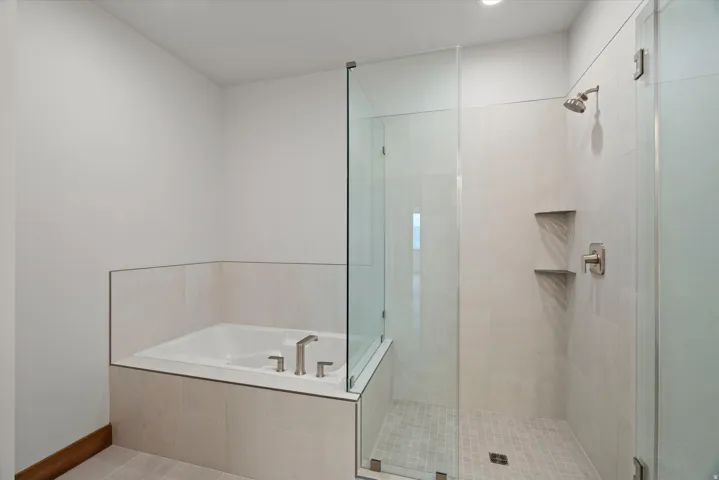 Spa-inspired primary bathroom featuring a soaking tub with brushed nickel fixtures, a spacious walk-in shower with frameless glass enclosure and mosaic tile surround, dual built-in niches, and polished tile flooring throughout