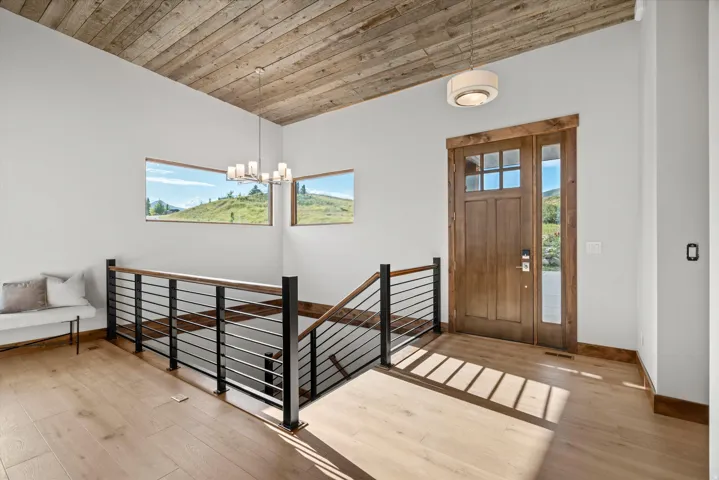 Modern mezzanine landing featuring warm wood-finish flooring, horizontal metal railing with black finish, recessed ceiling lighting, and expansive windows framing pastoral scenery