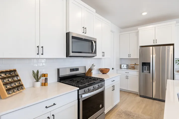 White cabinetry, stainless steel appliances, white subway tile backsplash, light-toned wood-finish flooring, and light-toned countertops