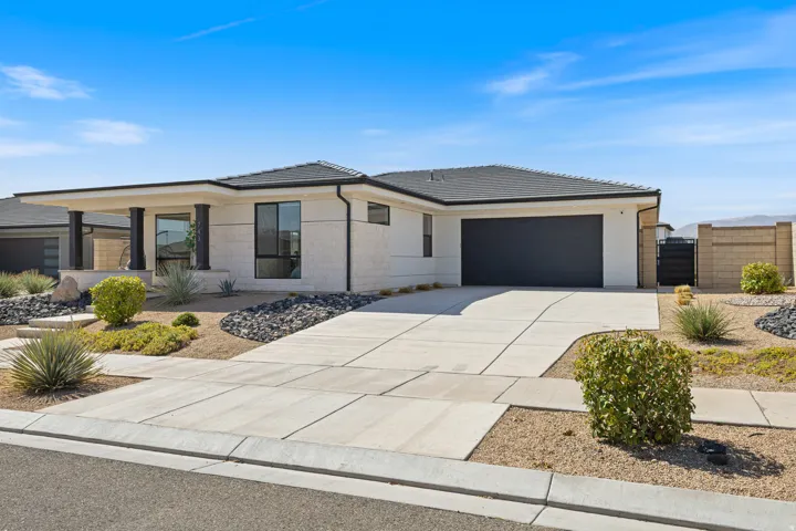 Single-story stucco exterior with a dark shingle roof, a two-car garage, an extended concrete driveway, and desert landscaping