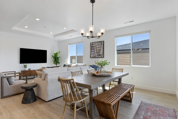 Recessed lighting, tray ceiling, two large windows, wood-finish flooring, and a modern chandelier