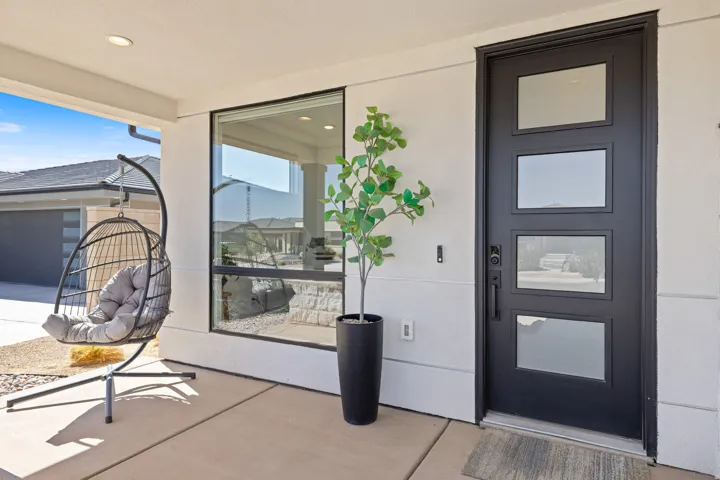 Contemporary black entry door with frosted glass panels, expansive fixed window with black trim, and a covered concrete patio