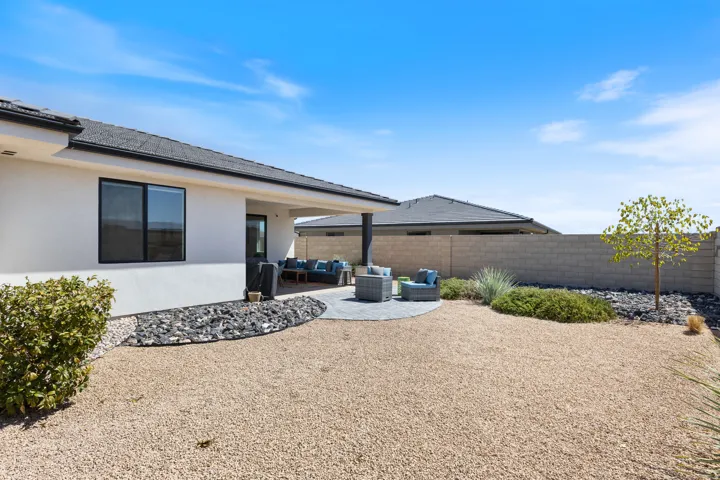 Expansive backyard with a covered patio, circular paver hardscaping, gravel landscaping, and a privacy wall