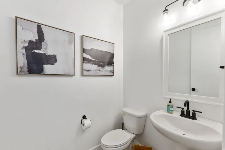 Pedestal sink with matte black faucet, wall-mounted mirror with white framing, and overhead vanity lighting