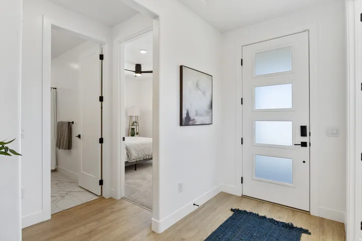 Bright entryway featuring wood-finish flooring, a glass-paneled exterior door with frosted upper panes, and direct access to a full bathroom and primary bedroom suite
