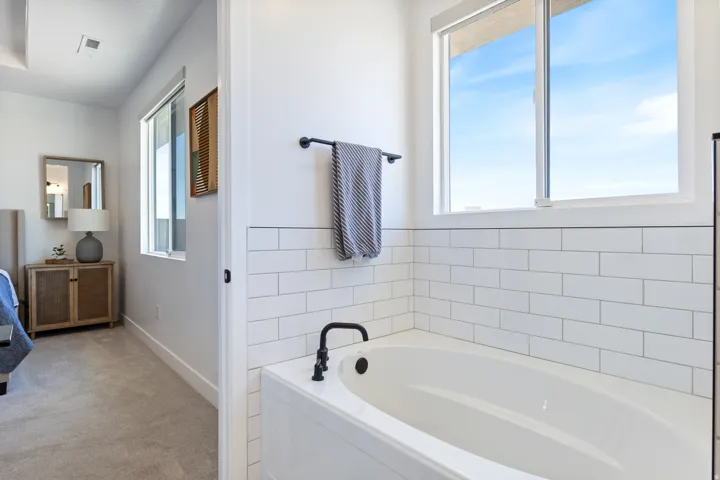 Built-in soaking tub with a matte black faucet and white subway tile surround, complemented by a large window