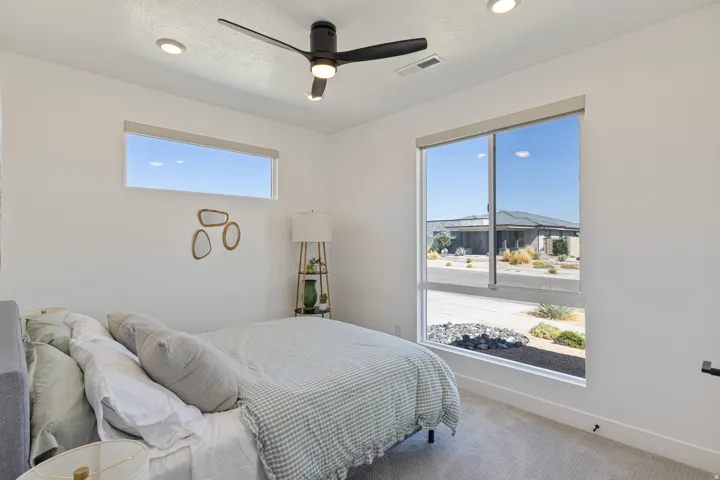 Bright corner bedroom with expansive windows framing skyline and mountain vistas, recessed ceiling lighting, and a modern ceiling fan with integrated light fixture