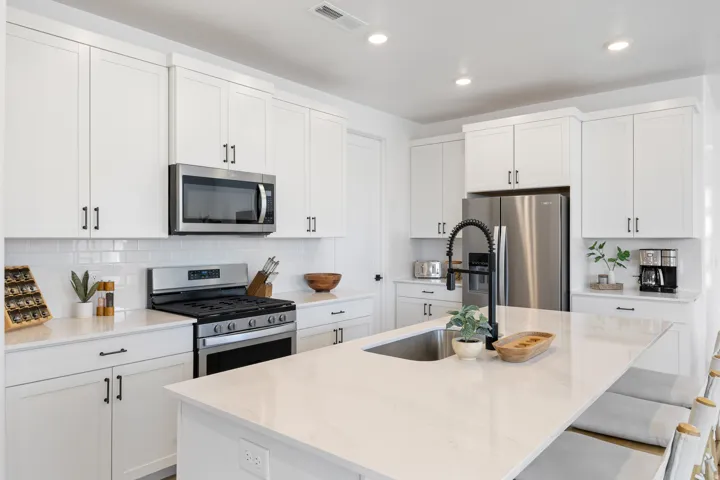 White shaker cabinetry, stainless steel appliances, white subway tile backsplash, light-toned countertops, and an undermount sink with a matte black faucet