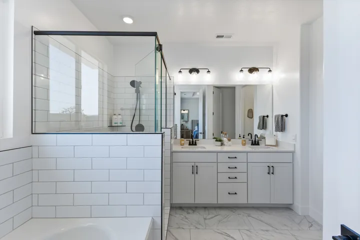 Spa-inspired primary bathroom featuring a frameless glass-enclosed shower with subway tile surround, dual-sink vanity with soft-close cabinetry and brushed nickel hardware, marble-look flooring, and contemporary lighting fixtures above the mirror