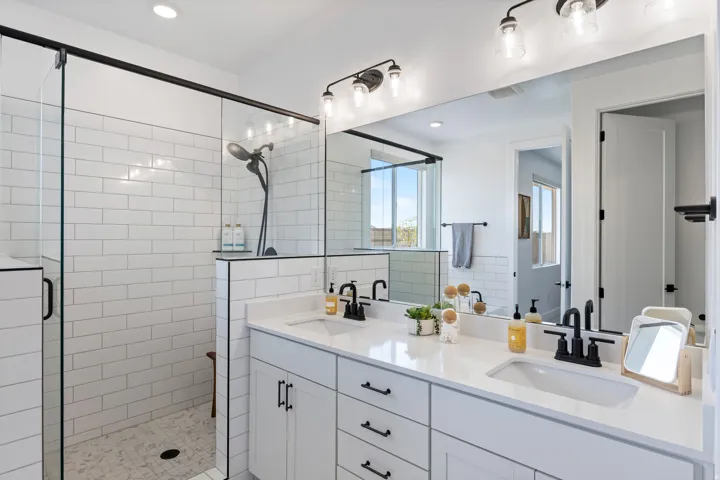 Dual vanity with undermount sinks and matte black fixtures, full-width mirror, walk-in shower with subway tile surround, clear glass shower enclosure, and recessed lighting