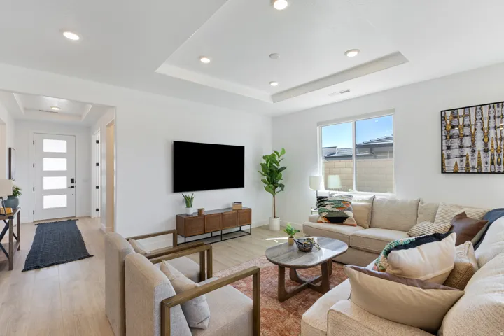 Recessed lighting throughout, tray ceiling detail, wood-finish flooring, ample natural light from large window, and a modern entry door with frosted glass panels