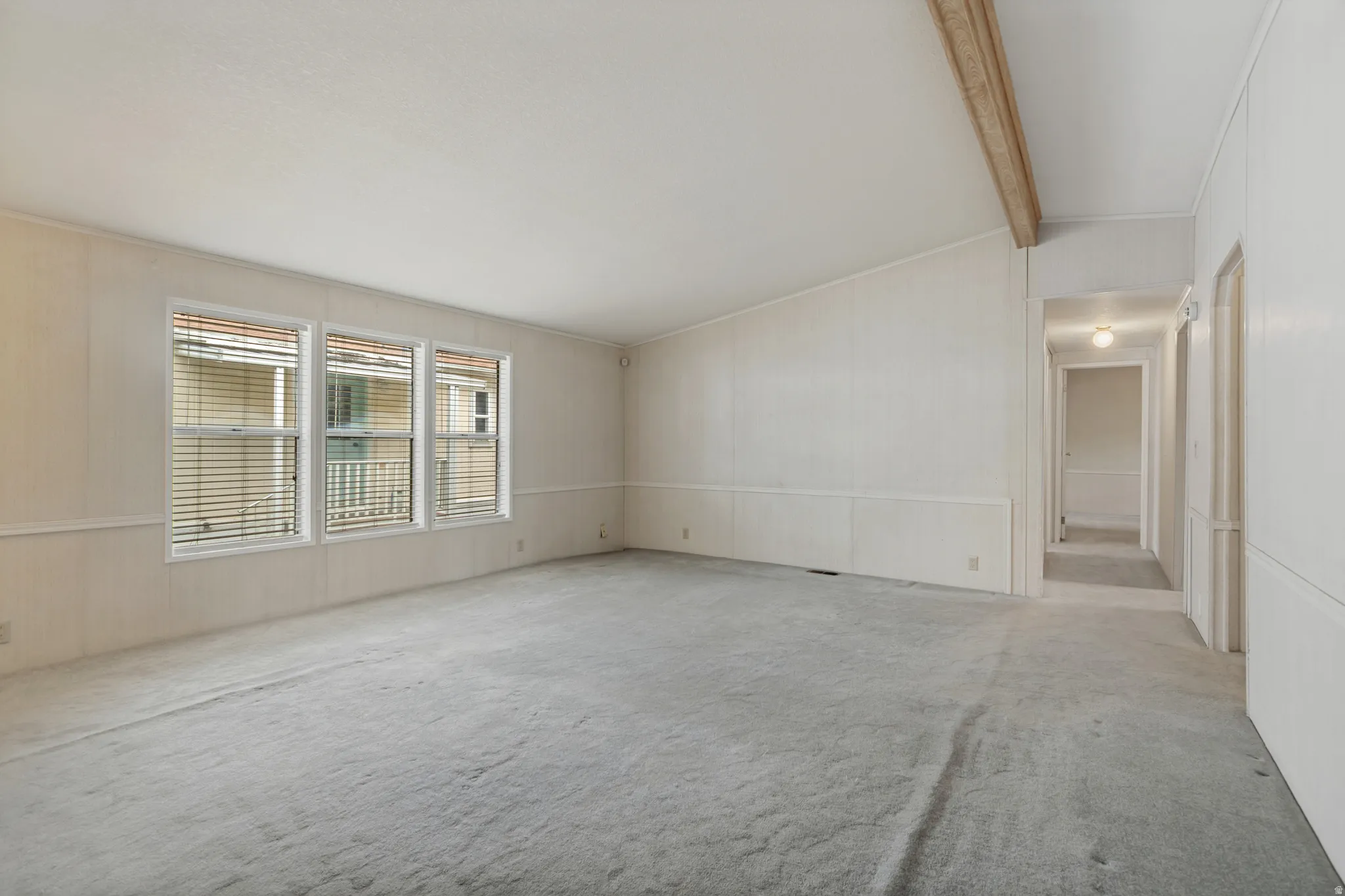 Vaulted ceiling with exposed wood beam, three windows, wall paneling, and a hallway with overhead lighting