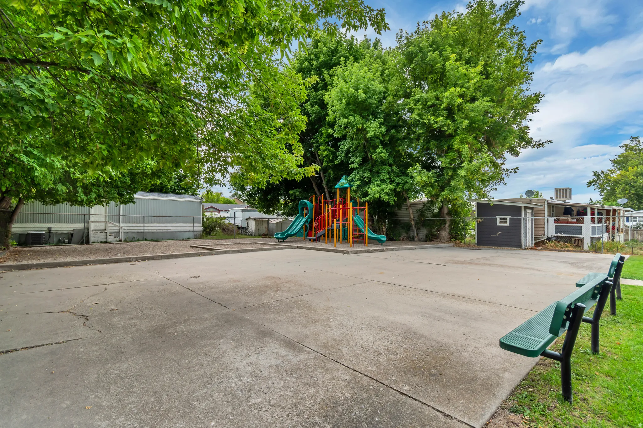 Community recreation area featuring a playground structure with slides, concrete paving, and green benches