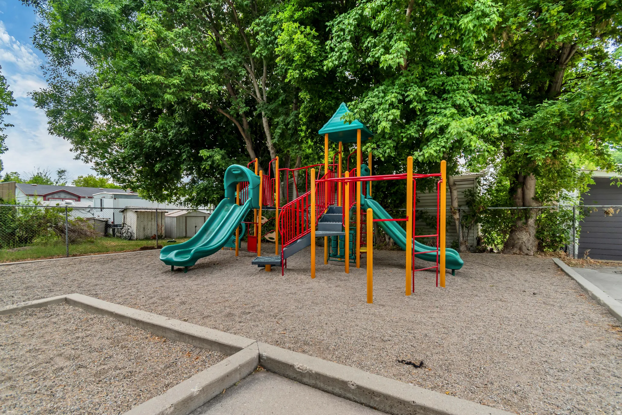 Playground structure with multiple slides, climbing elements, and overhead bars set on a gravel surface
