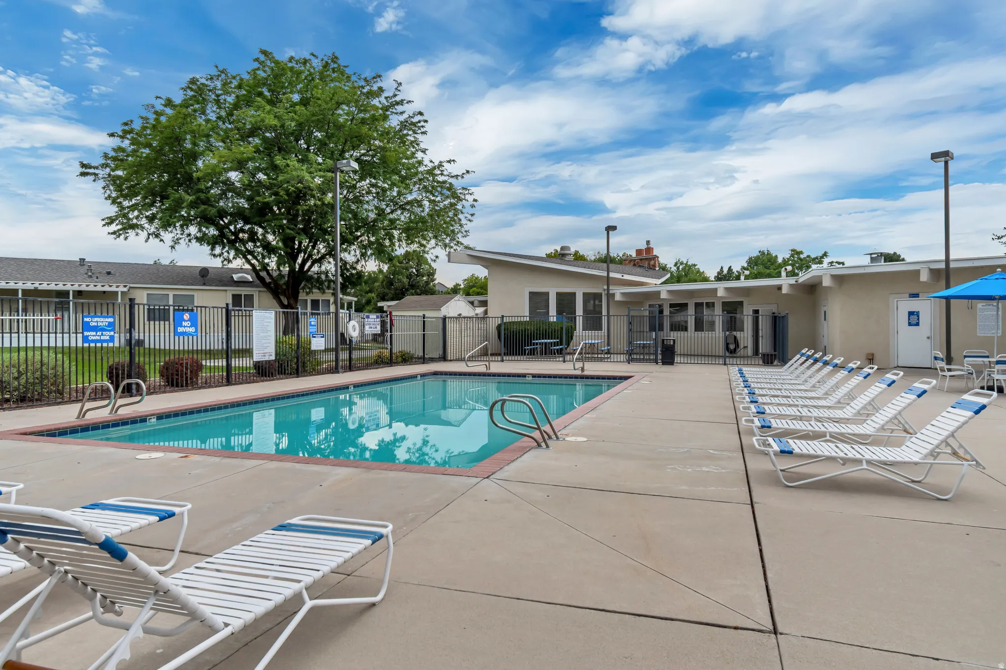 Outdoor swimming pool with concrete decking, perimeter fencing, and surrounding low-rise buildings