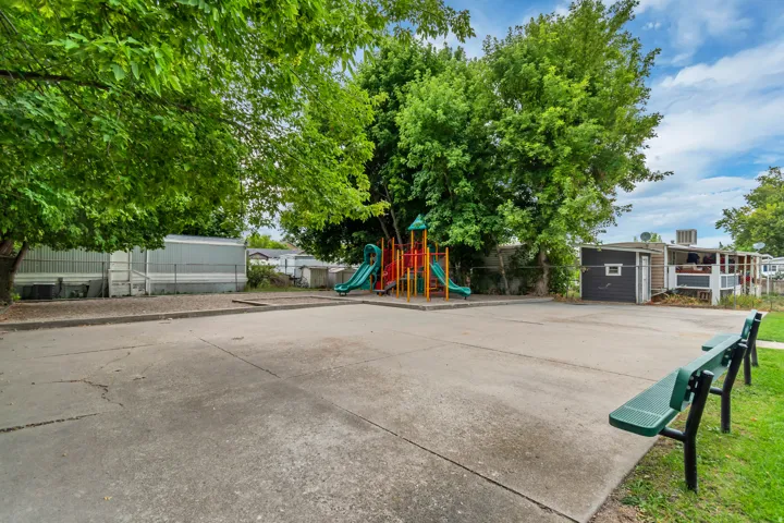Community recreation area featuring a playground structure with slides, concrete paving, and green benches
