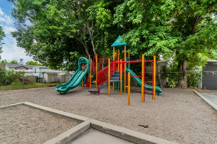 Playground structure with multiple slides, climbing elements, and overhead bars set on a gravel surface