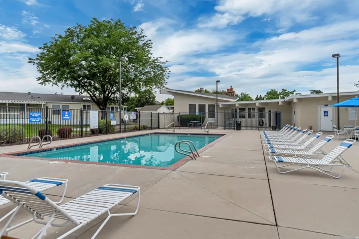 Outdoor swimming pool with concrete decking, perimeter fencing, and surrounding low-rise buildings