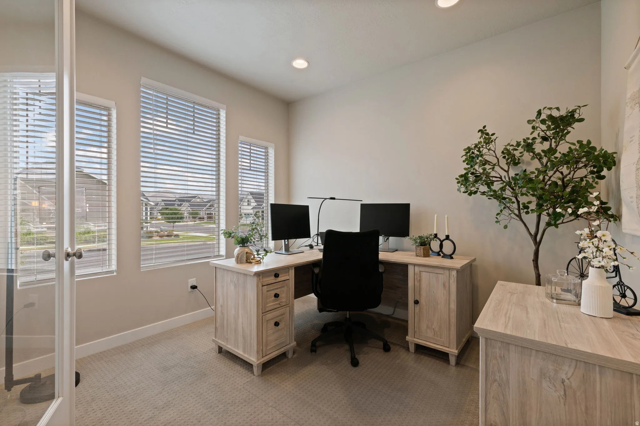 Recessed ceiling lighting, multiple windows with blinds, light-toned carpeting, and a glass-paneled entry door
